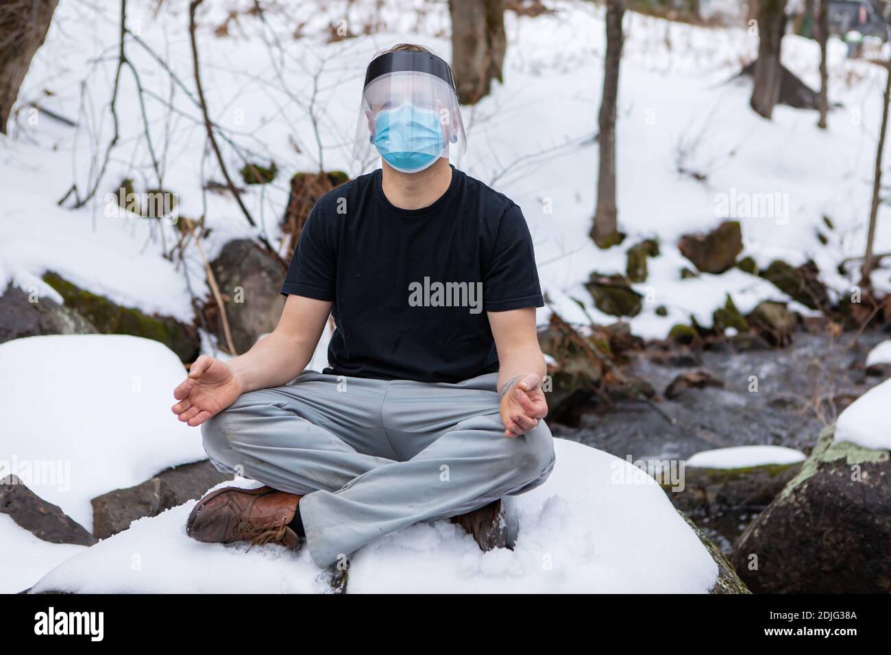 Scatto frontale completo dell'uomo in una t-shirt seduta nella posizione  yoga fiore di loto su una grande roccia nella neve, indossando maschera  covid e visiera protettiva Foto stock - Alamy