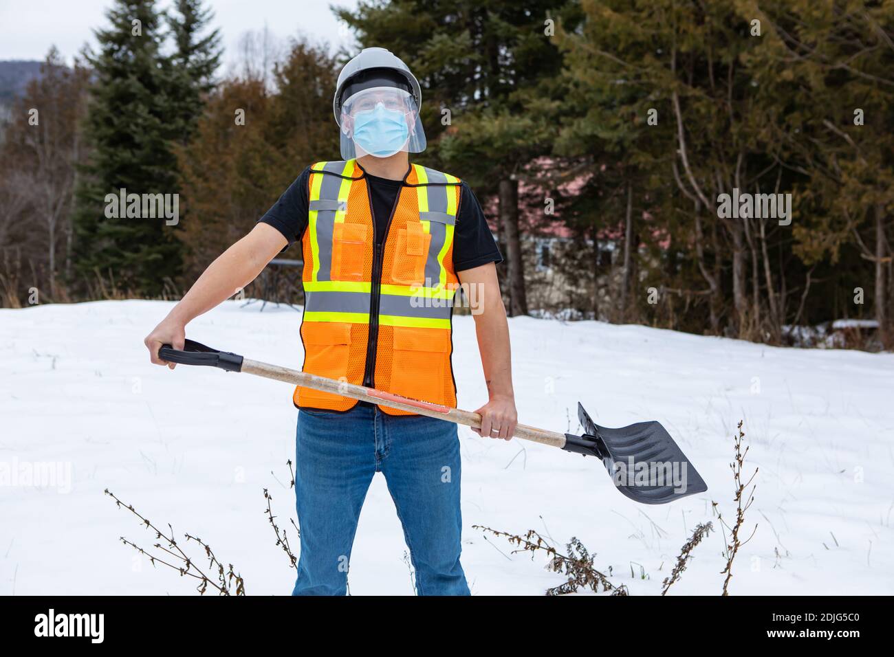 Foto media di un uomo che indossa una giacca arancione fluo visibility sopra una t-shirt, una maschera protettiva per il viso e una visiera in plastica, che tovola la neve Foto Stock