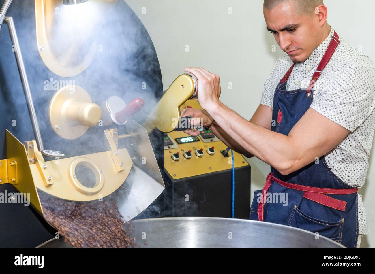 Le mani dell'uomo arrostire i chicchi di caffè aromatico su un moderno macchina utilizzata per tostare i fagioli Foto Stock