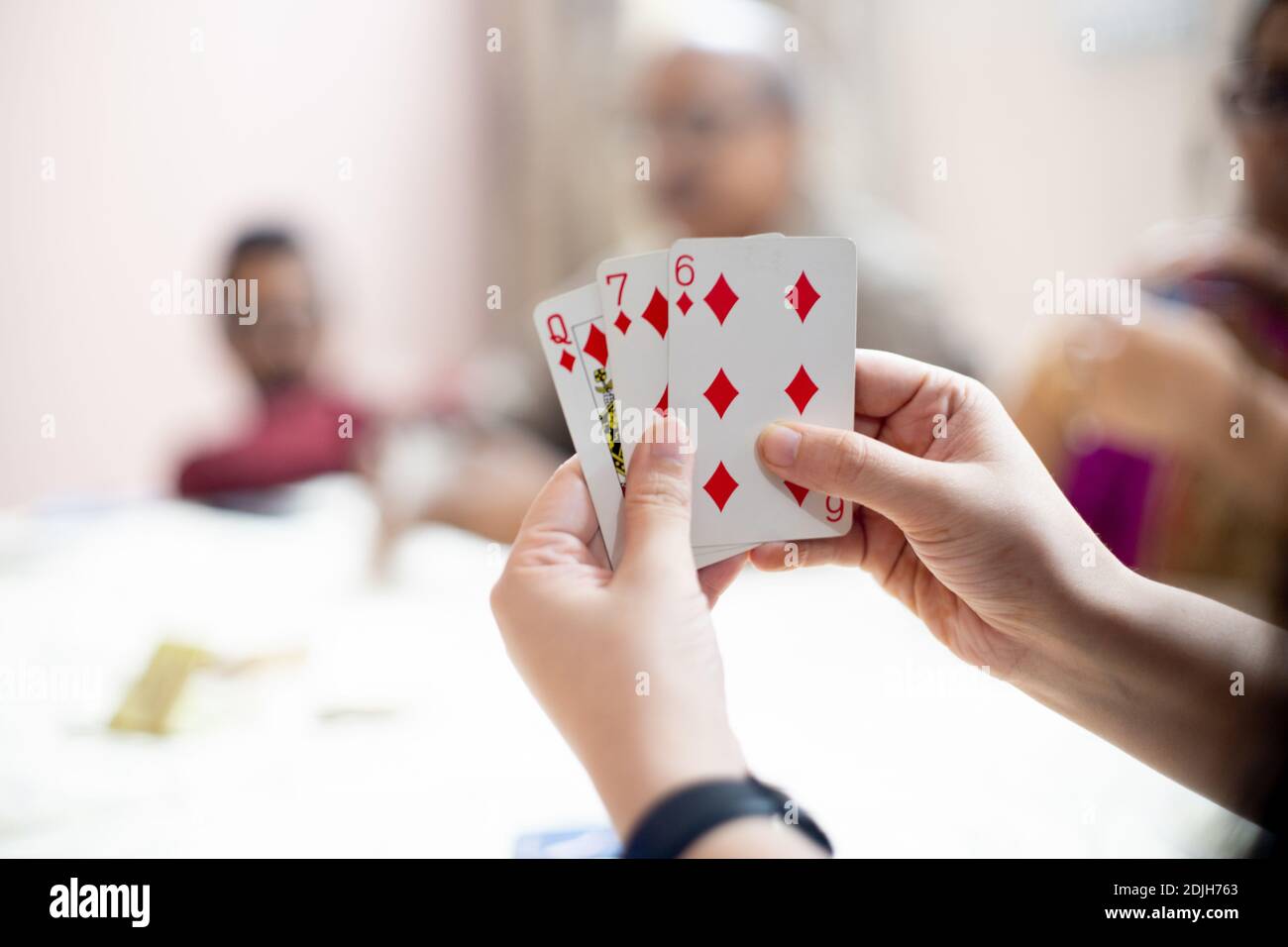 Donna che tiene le carte con i membri della famiglia fuori fuoco a distanza che mostra una famiglia che gioca le carte su festival come diwali, dussera, anno nuovo e. Foto Stock