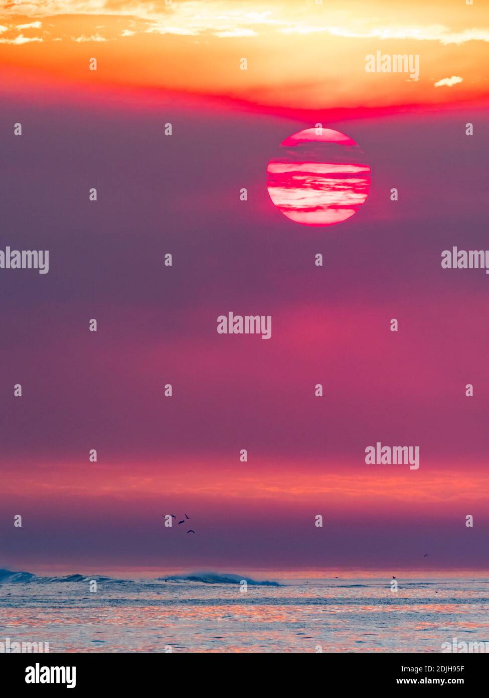 Il sole tramonta sul surf a la Jolla Shores, California, con fumo da un fuoco durante i venti di Santa Ana Foto Stock