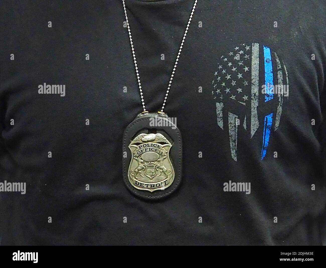 Il badge della polizia di Detroit è appeso al collo di un ufficiale su una catena, su una bandiera americana e una t-shirt con motivo Thin Blue Line Foto Stock