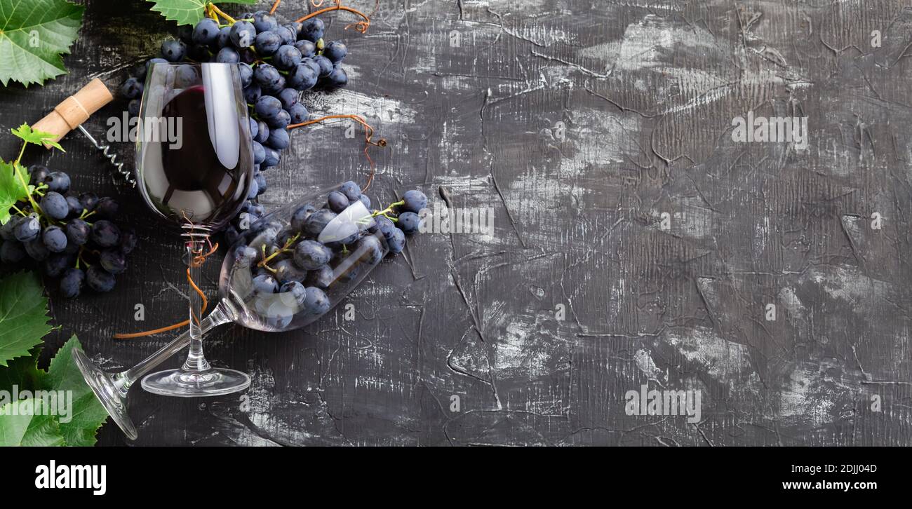 Bicchieri da vino con vino rosso e uva. Grappoli d'uva con foglie e tappi di vite su fondo di cemento rustico scuro. Composizione di vino piatto su blac Foto Stock
