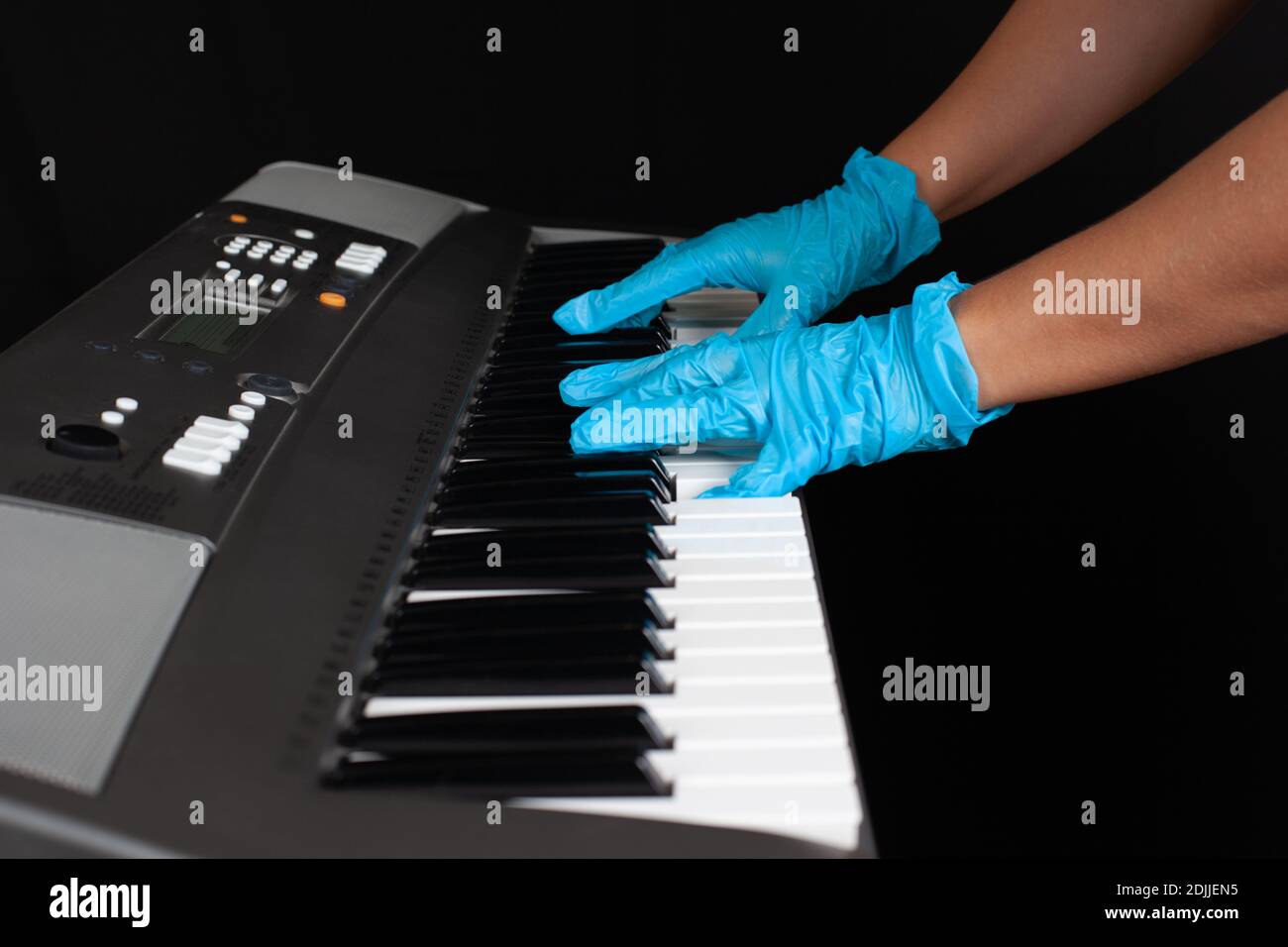 primo piano delle mani femminili in guanti di protezione blu che giocano una melodia sulle chiavi di un sintetizzatore elettronico, un simbolo o un concetto di protezione della salute Foto Stock