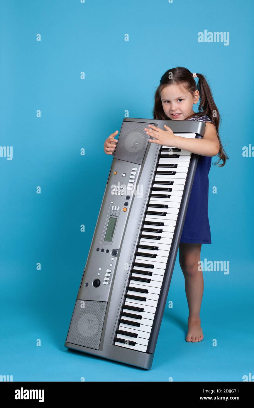 Ritratto di una ragazza sorridente che abbraccia un sintetizzatore elettronico verticale, Studio isolato su sfondo blu Foto Stock