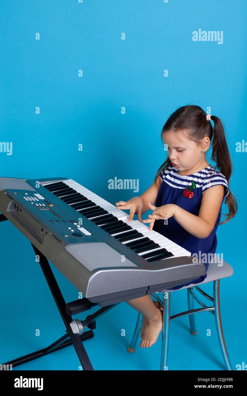 ragazza interessata a tutta lunghezza che suona una melodia sulle chiavi di un sintetizzatore elettronico, formazione a distanza, isolata su sfondo blu Foto Stock