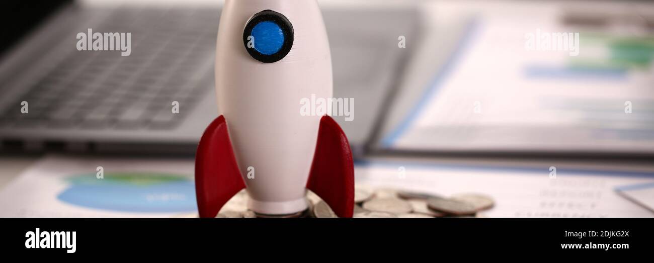 Razzo giocattolo, monete e penna d'argento sul tavolo Foto Stock