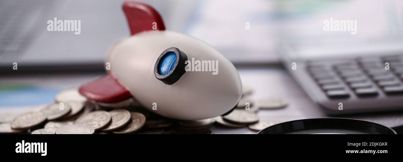 Razzo giocattolo, monete, penna d'argento e lente d'ingrandimento sul tavolo Foto Stock