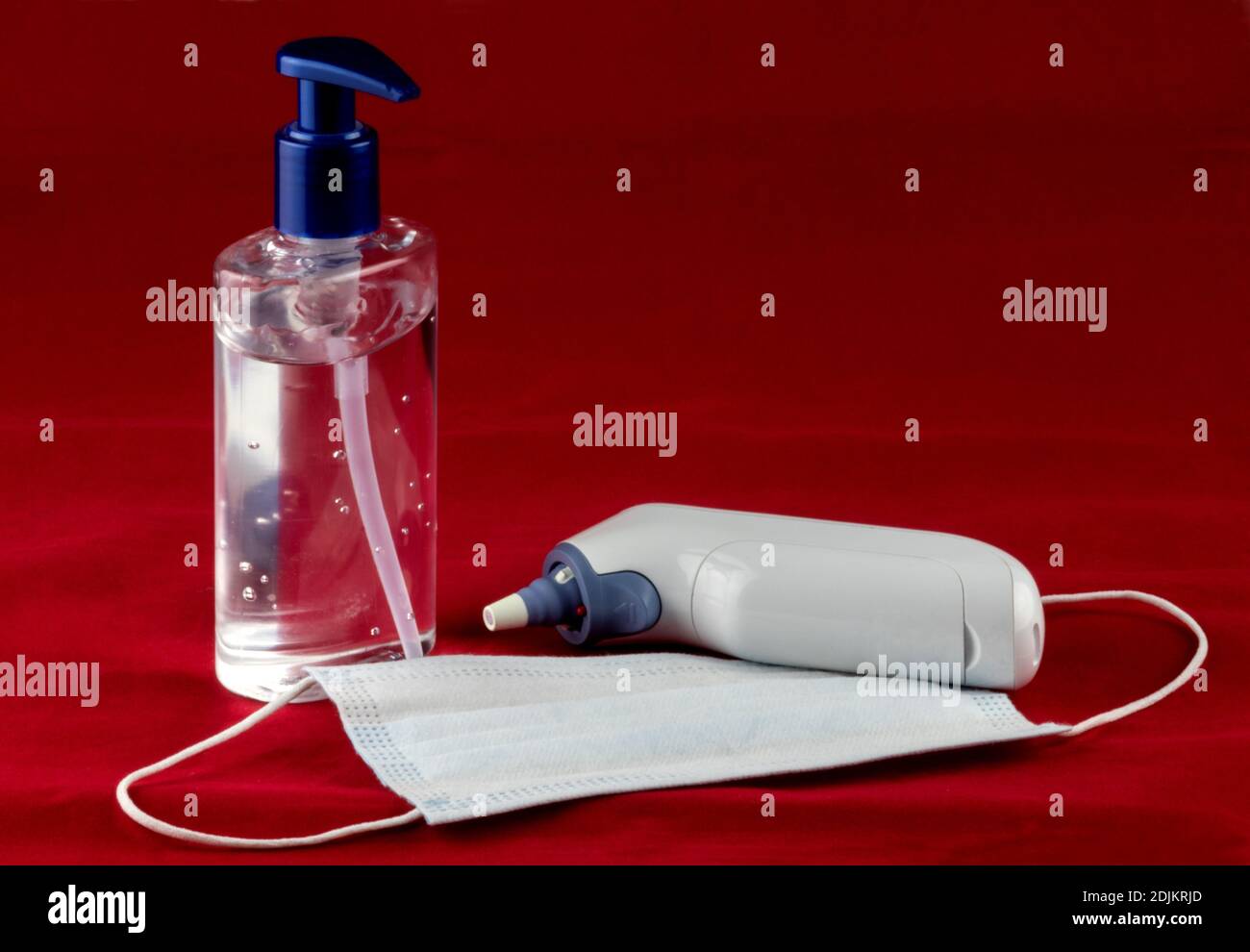 Maschera facciale disinfettante per le mani e termometro auricolare su un rosso tessuto di fondo Foto Stock