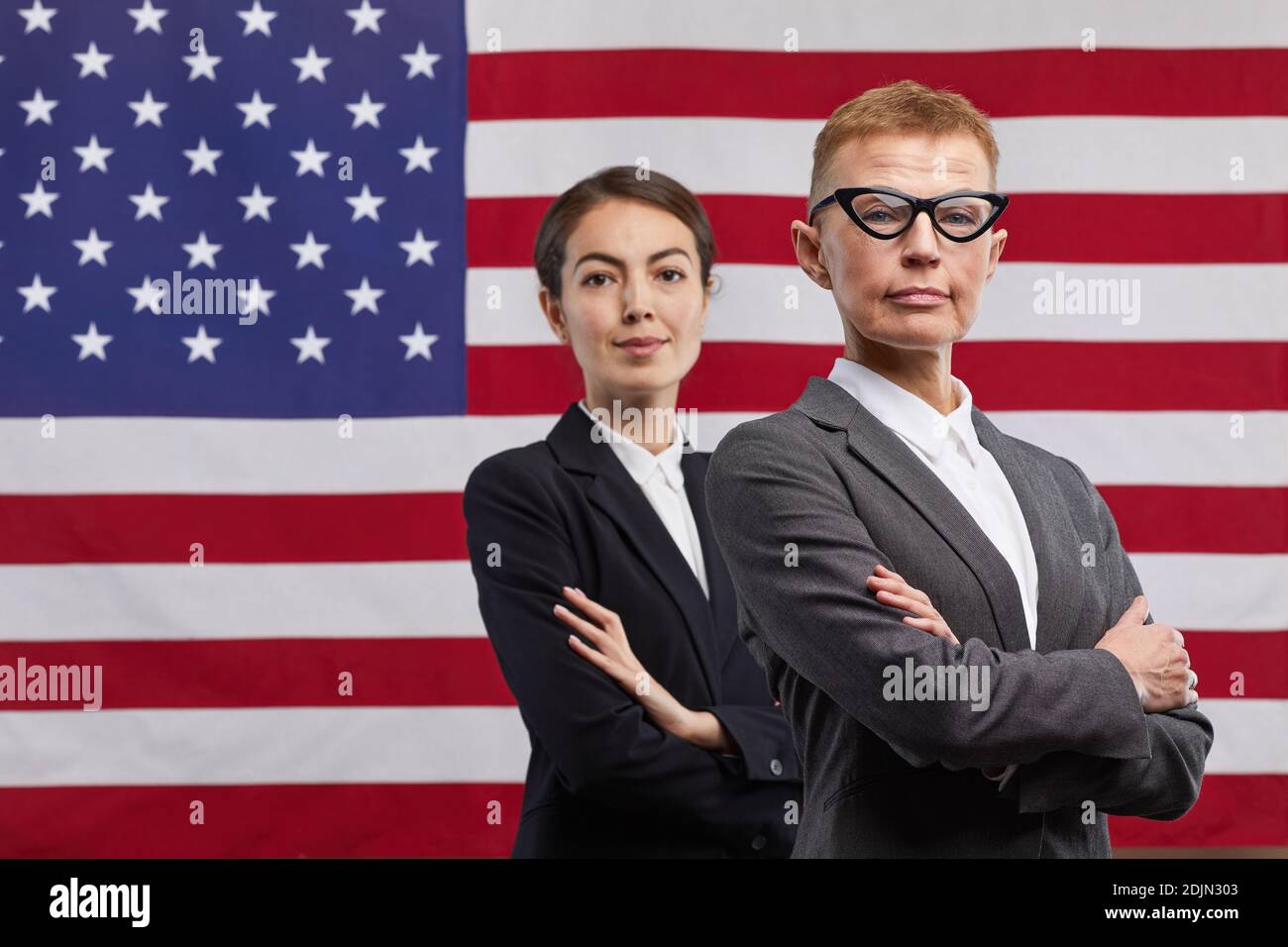 Vita in su ritratto di due politici fidati donne guardando la macchina fotografica mentre si è in piedi con le braccia incrociate contro lo sfondo della bandiera degli Stati Uniti, copia spazio Foto Stock