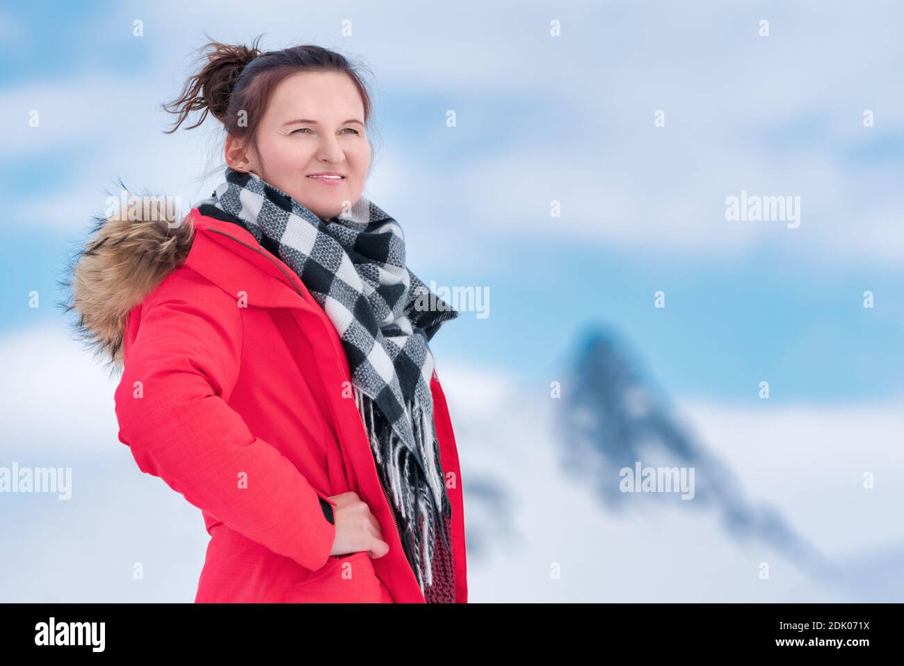 Ritratto di donna viaggiatore vestito con giacca antivento invernale rossa, sciarpa nera e bianca intorno al collo. Donna misteriosa sullo sfondo delle montagne Foto Stock