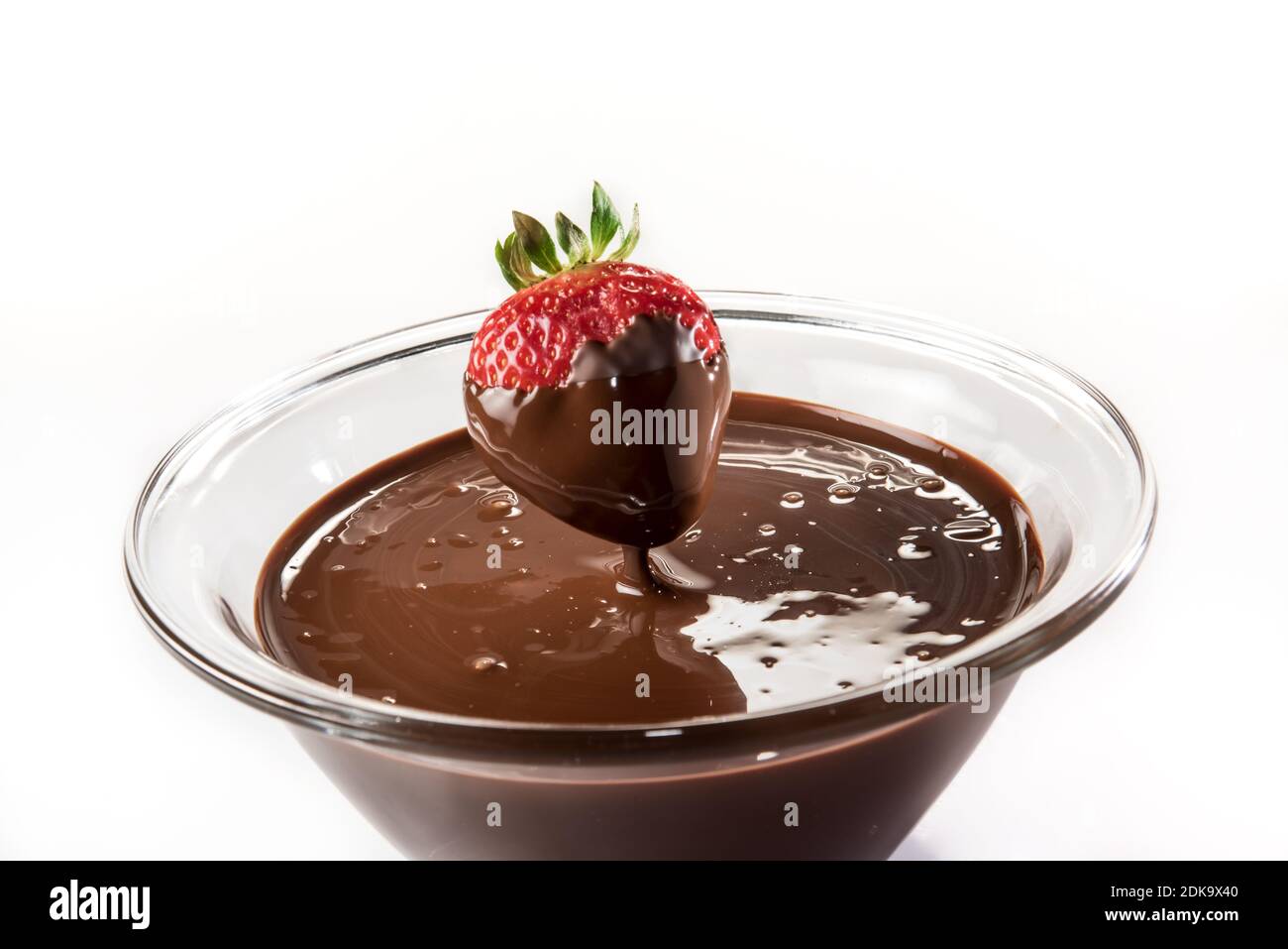 Il cioccolato gocciola dalla fragola in una tazza di vetro con il colore scuro fuso cioccolato su sfondo bianco Foto Stock