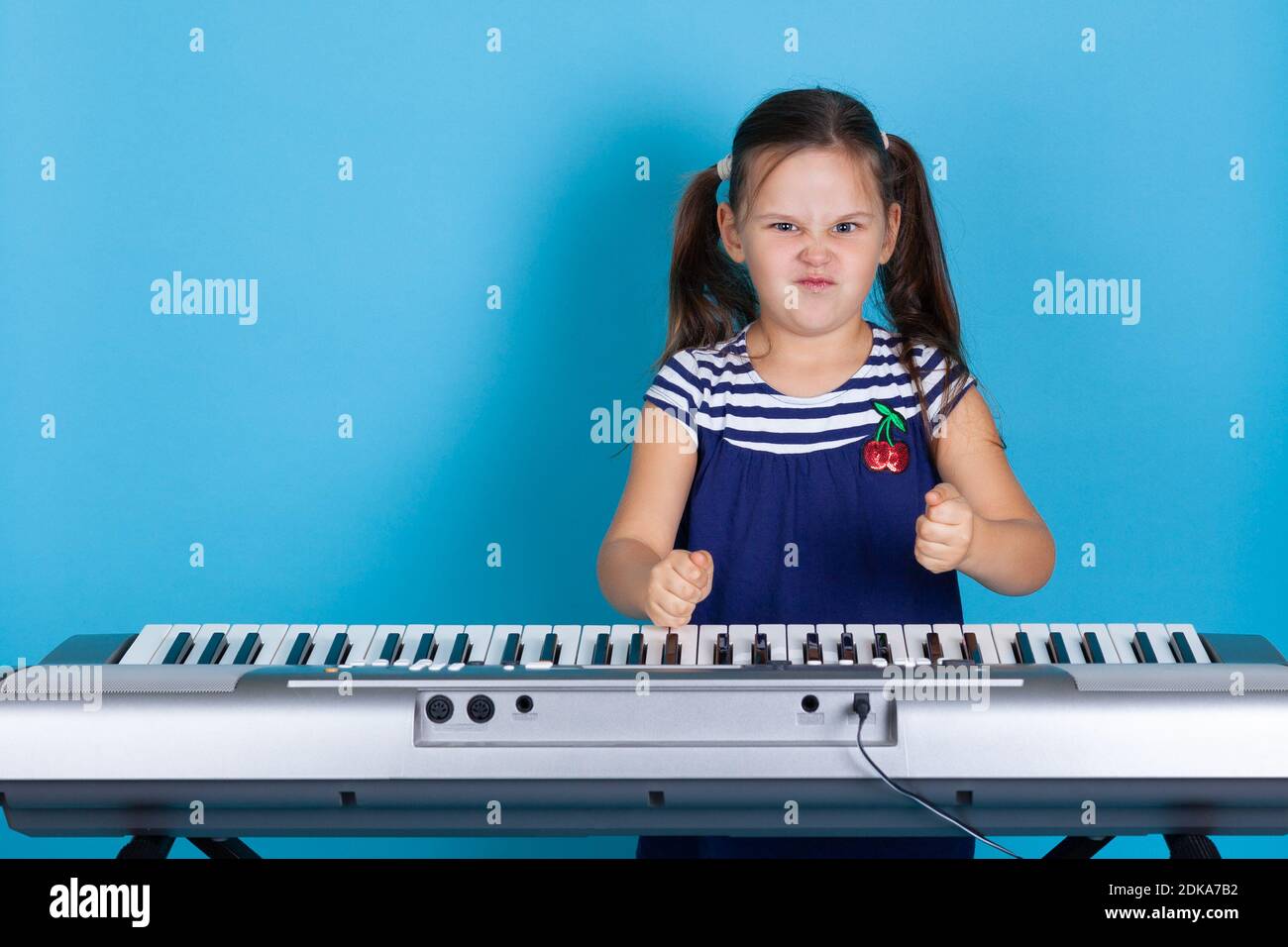 fock up scowling ragazza banging i suoi pugni sui tasti del sintetizzatore, odorando la musica classica, isolato su sfondo blu Foto Stock