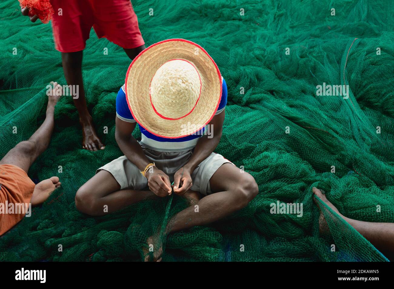 Pescatore indentificato, indossando cappello luminoso, riparando grande rete di pesca verde con le mani e i piedi in Kannur, Kerala, India. Foto Stock