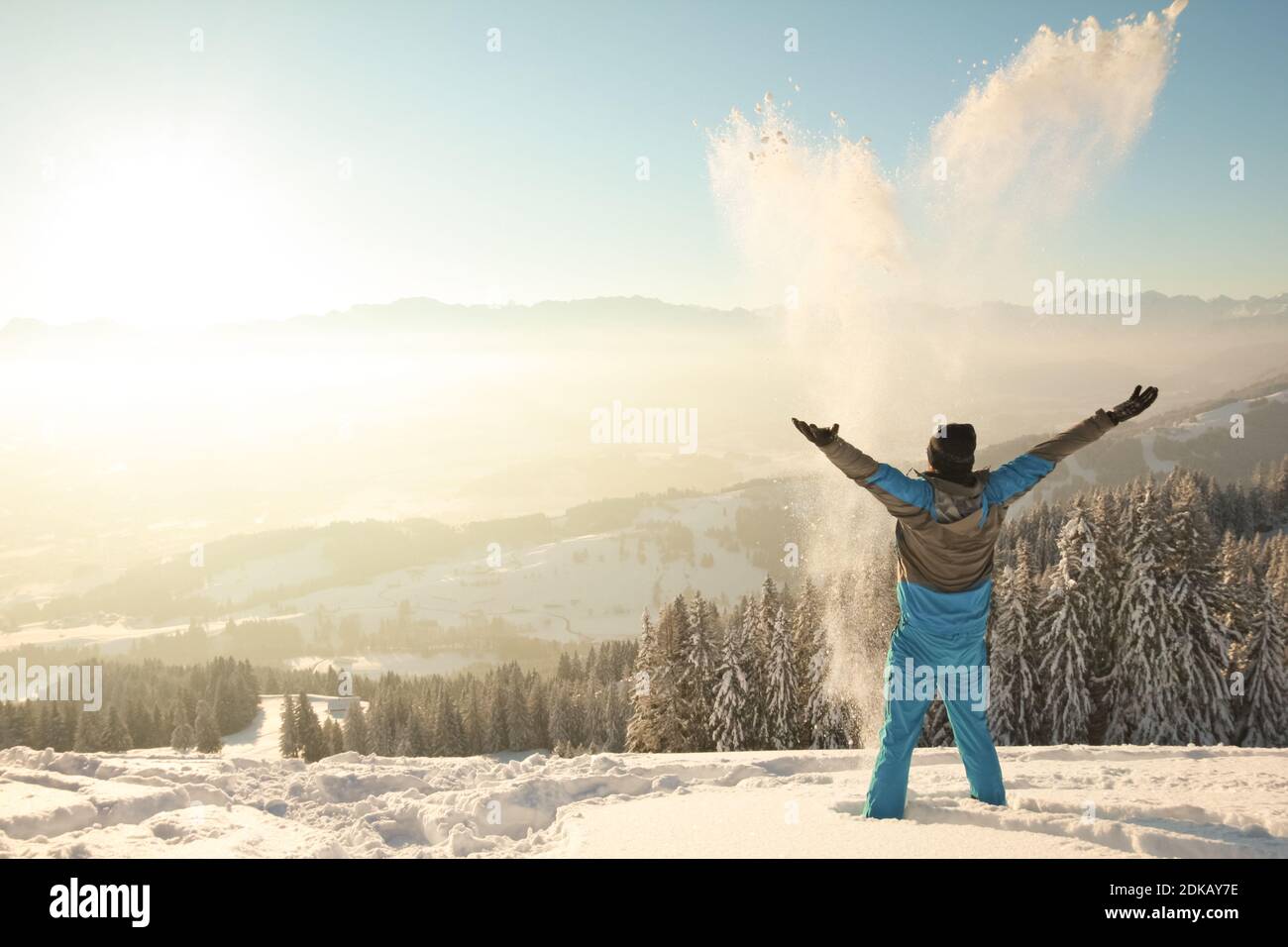 Happy Man in piedi nella neve profonda gettando la neve nella luce solare dell'alba. Splendido paesaggio invernale. Allgau, Baviera, Alpi, Germania. Foto Stock