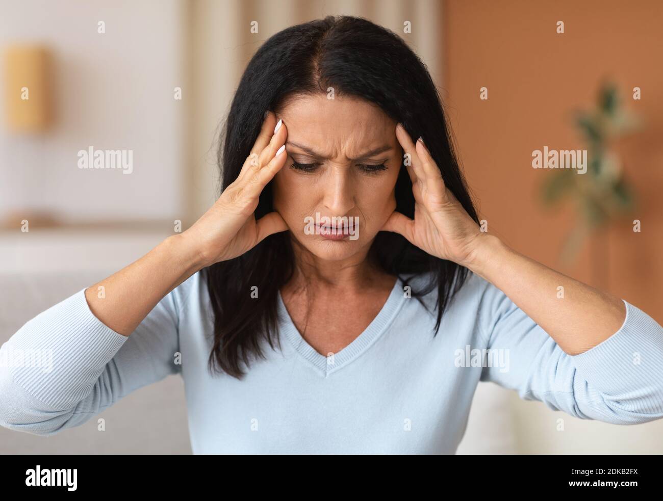 Donna bruna matura che tocca i suoi templi sensazione di mal di testa Foto Stock