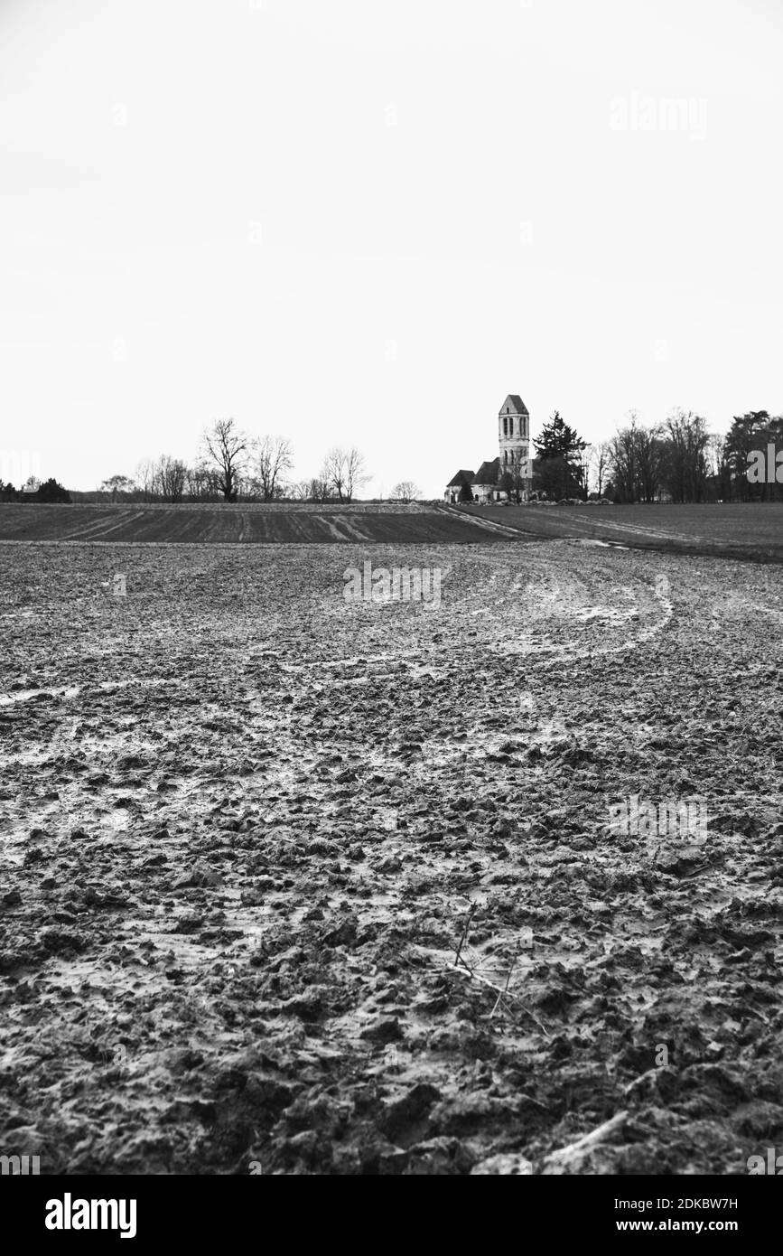 Paesaggi della Francia. Campo arato dopo la pioggia e vecchia chiesa sullo sfondo a Luzarches, Val-d'Oise, Ile-de-France. Foto storica in bianco nero. Foto Stock