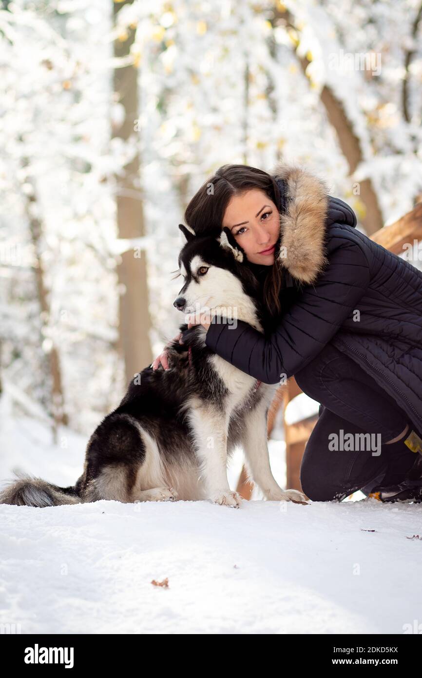 Bella giovane donna abbracciando femmina Husky cane in freddo inverno nevoso giorno. Foto di alta qualità Foto Stock