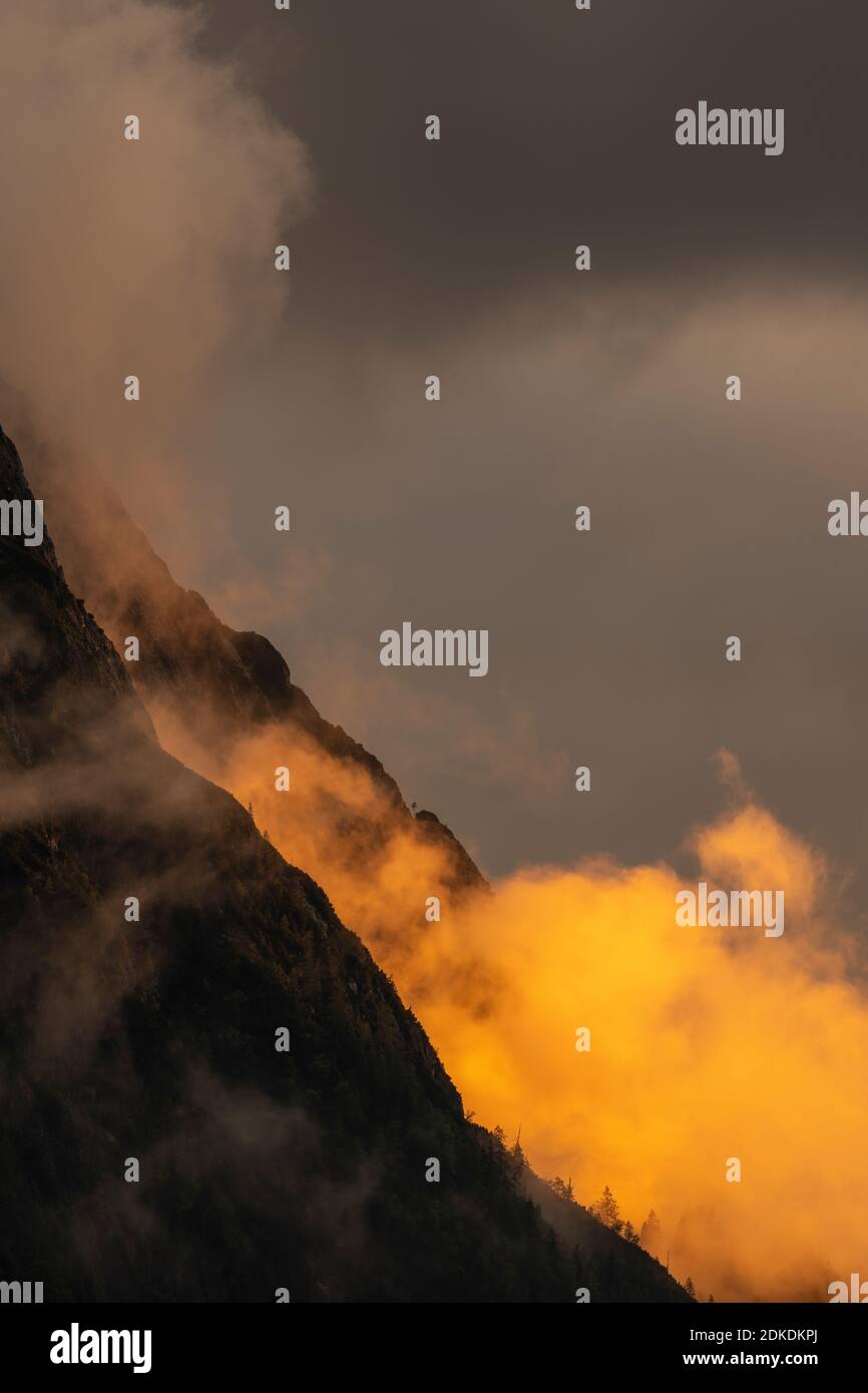 Alpenglow ai piedi del Wetterstein, sopra Mittenwald. Atmosfera di nube e roccia drammatica delle montagne, con alberi e tonalità arancio. Foto Stock