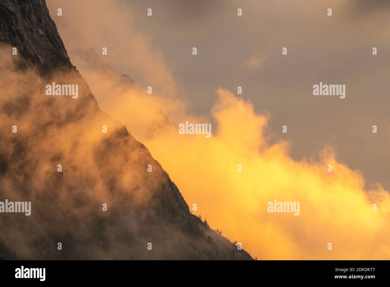 Alpenglow ai piedi del Wetterstein, sopra Mittenwald. Atmosfera di nube e roccia drammatica delle montagne, con alberi e tonalità arancio. Foto Stock