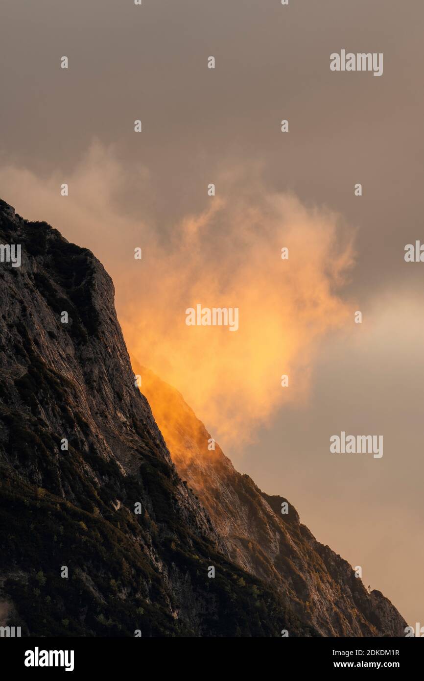 Alpenglow ai piedi del Wetterstein, sopra Mittenwald. Atmosfera di nube e roccia drammatica delle montagne, con alberi e tonalità arancio. Foto Stock