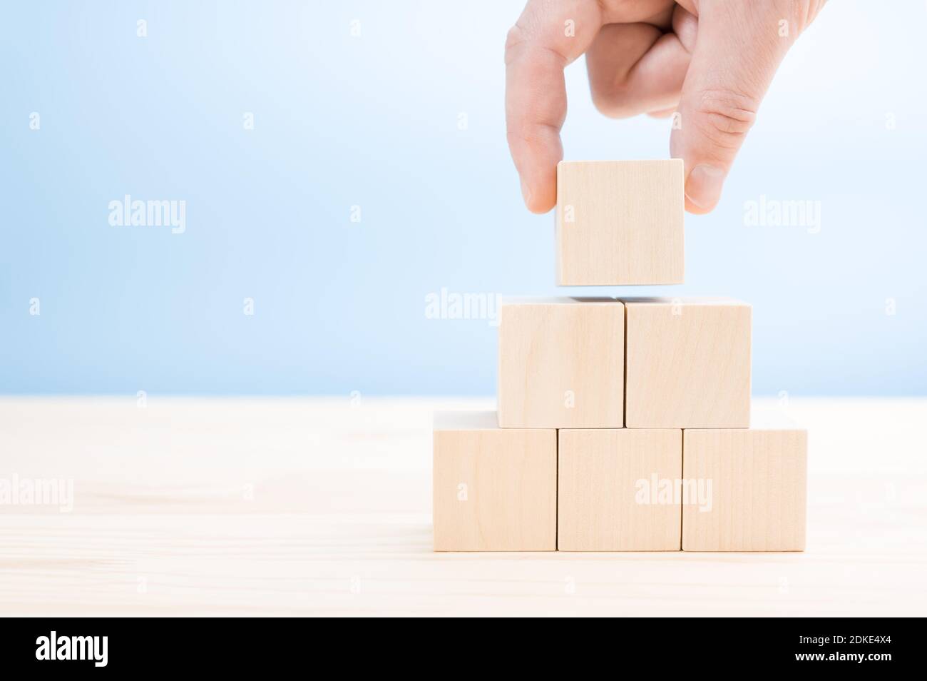 la mano si presenta costruisce una piramide di cubi di legno vergini. Un blocco di legno a forma di cubo impilato a forma di piramide senza grafica per il concetto di progettazione aziendale. Foto Stock