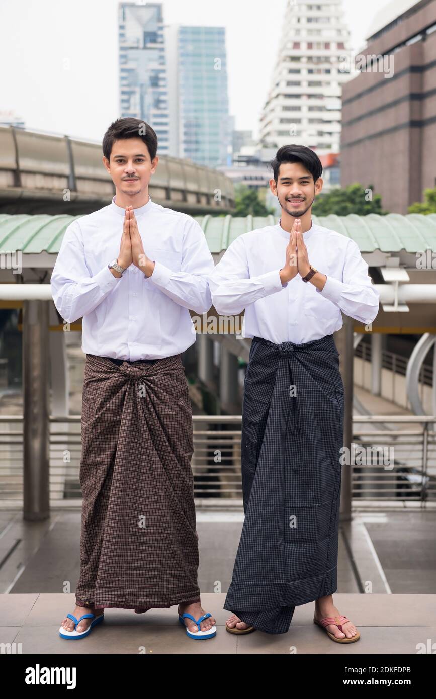 Ritratto di bei birmani o Myanmar uomini con abito tradizionale longyi  eseguire il saluto o pagare segno di rispetto mano nella città moderna.  Ragazzi intelligenti sorridenti in costume tradizionale. Tradizionale gesto  di