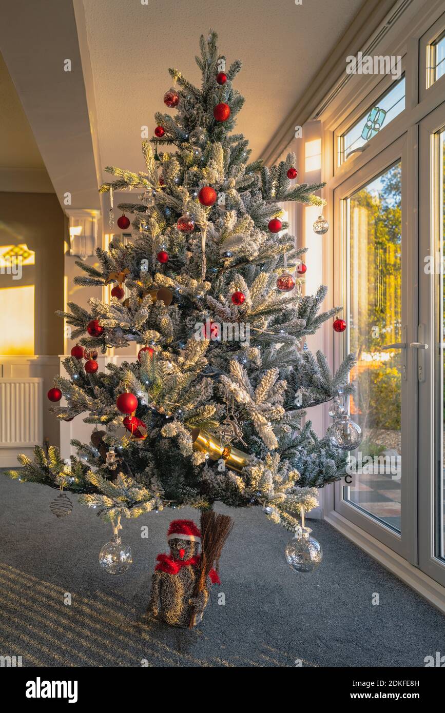 Un albero di natale artificiale ghiacciato con decorazioni e luci fiabe di fronte alle porte del patio durante l'inizio di un tramonto. Foto Stock