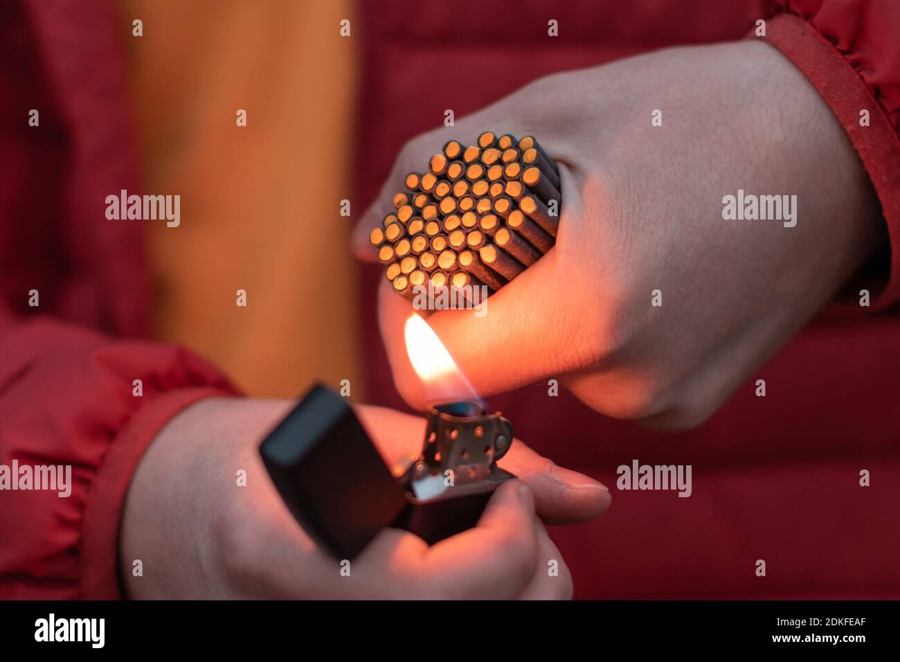 L'uomo in rosso ha sollevato l'illuminazione molti piccoli Firecrackers neri nella sua mano usando l'accendino a benzina. Guy prepararsi per il divertimento di Capodanno con fuochi d'artificio o prodotti pirotecnici Foto Stock