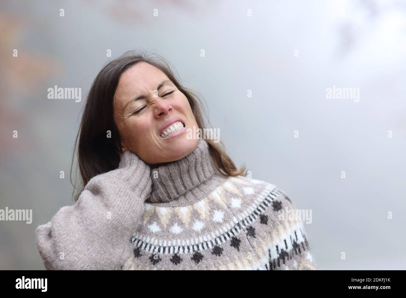 Donna di mezza età che soffre mal di collo in un freddo e. giorno invernale foggy Foto Stock