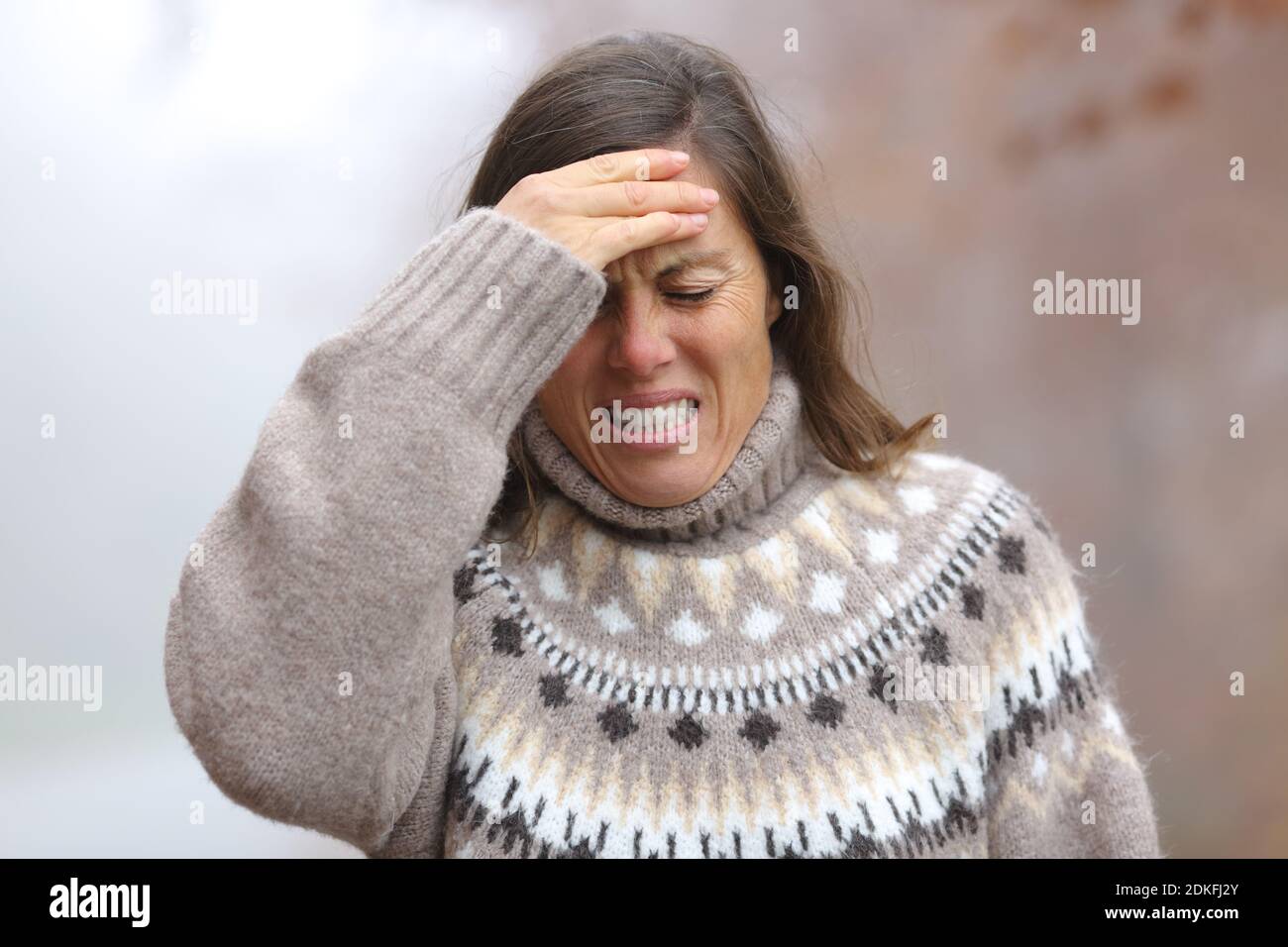 Donna adulta che soffre mal di testa a piedi in un parco dentro una fredda giornata invernale Foto Stock
