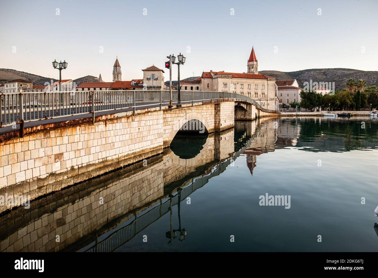 Il ponte per la città vecchia di Trogir, Croazia. La città è patrimonio dell'umanità dell'UNESCO. L'immagine mostra l'acqua calma intorno al ponte all'ora del mattino. Sullo sfondo si può vedere la torre della Cattedrale di San Lorenzo. Foto Stock