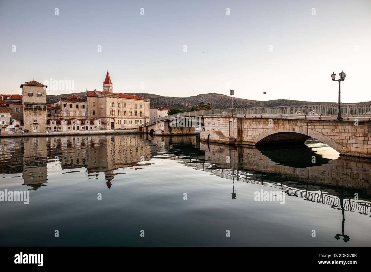 Il ponte per la città vecchia di Trogir, Croazia. La città è patrimonio dell'umanità dell'UNESCO. L'immagine mostra l'acqua calma intorno al ponte all'ora del mattino. Sullo sfondo si può vedere la torre della Cattedrale di San Lorenzo. Foto Stock
