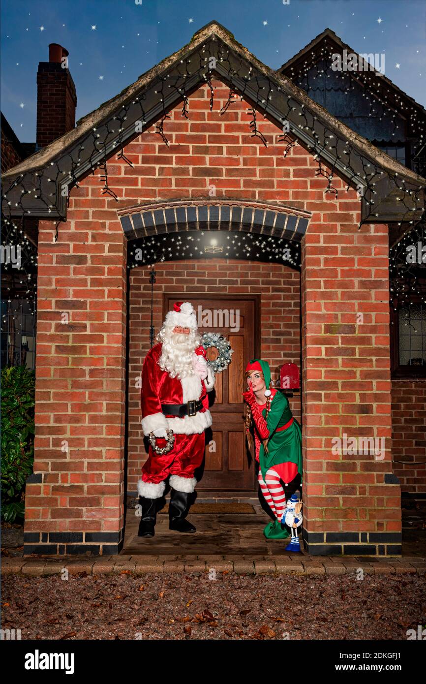 Regno Unito, Quorn - Dicembre 2020: Santa e un Elf si sbirciano fino a una porta d'ingresso mentre consegnano i regali Foto Stock