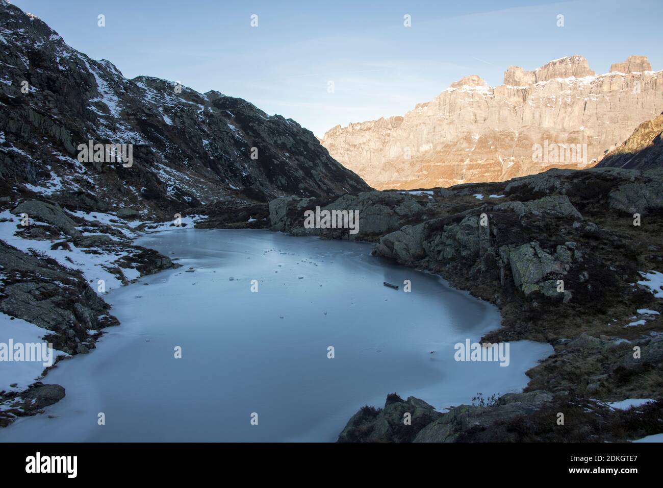 lago di montagna ghiacciato all'ombra, di fronte al lato di montagna nella prima luce solare Foto Stock