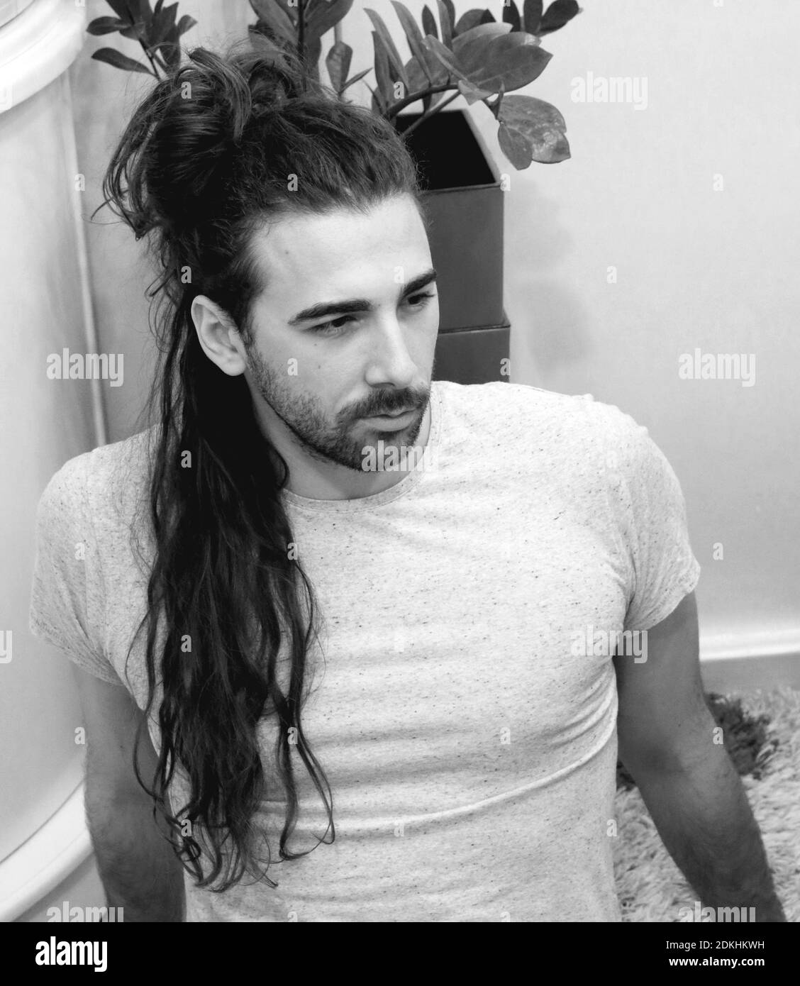 Attraente, giovane modello maschio con i capelli lunghi che si posano all'interno. Stile, tendenze, concetto di moda. Foto Stock