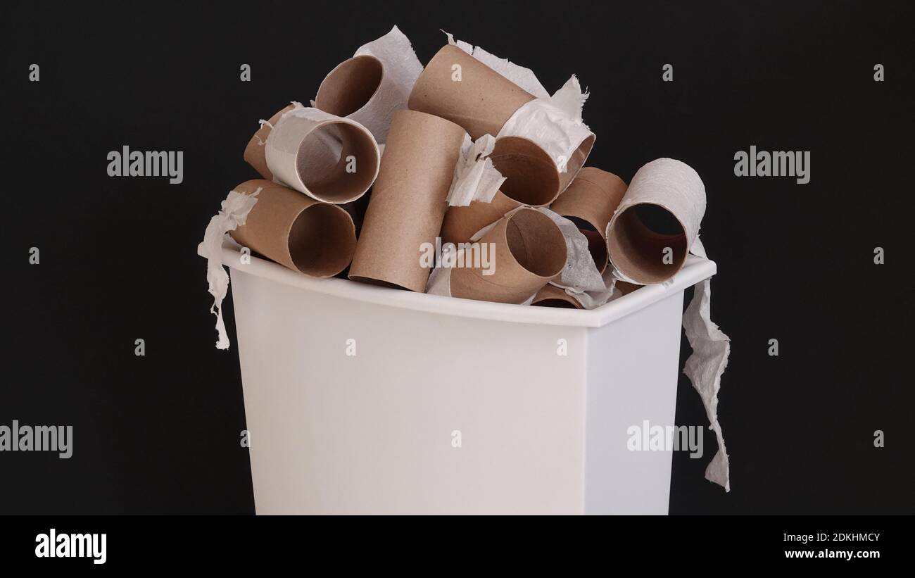 I rotoli di carta igienica di cartone usati e vuoti vengono mostrati impilati in un piccolo cestino, isolato su uno sfondo nero. Foto Stock