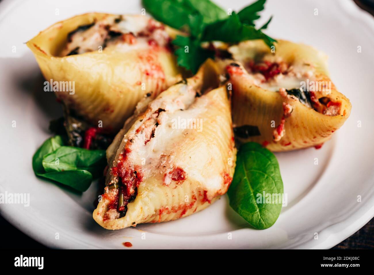 Conchiglie di jumbo al forno farcite con manzo macinato, spinaci e formaggio su piatto bianco Foto Stock