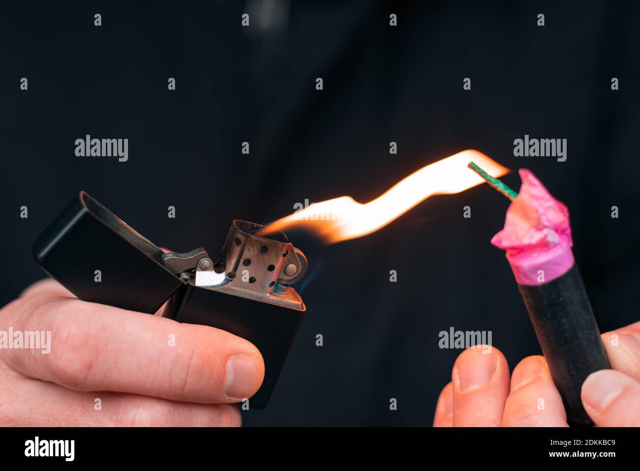 Impostazione di Fire sul Firecracker. Uomo in vestiti neri che illuminano il Petard. Accensione dei pirotecnici con un accendino a benzina nero all'aperto Foto Stock