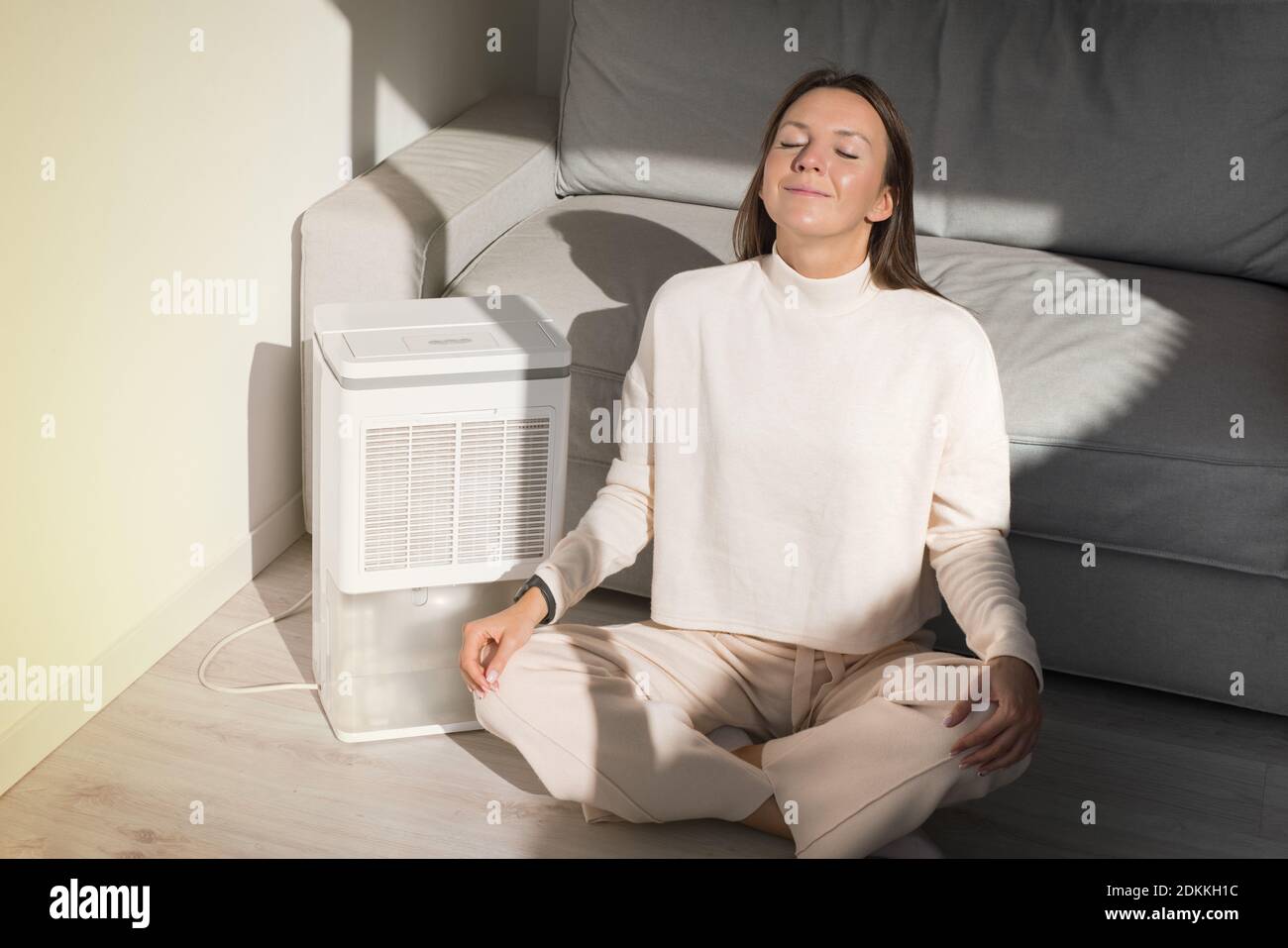 Donna calma con seduta vicino purificatore d'aria. Aria fresca rilassante e respirabile Foto Stock