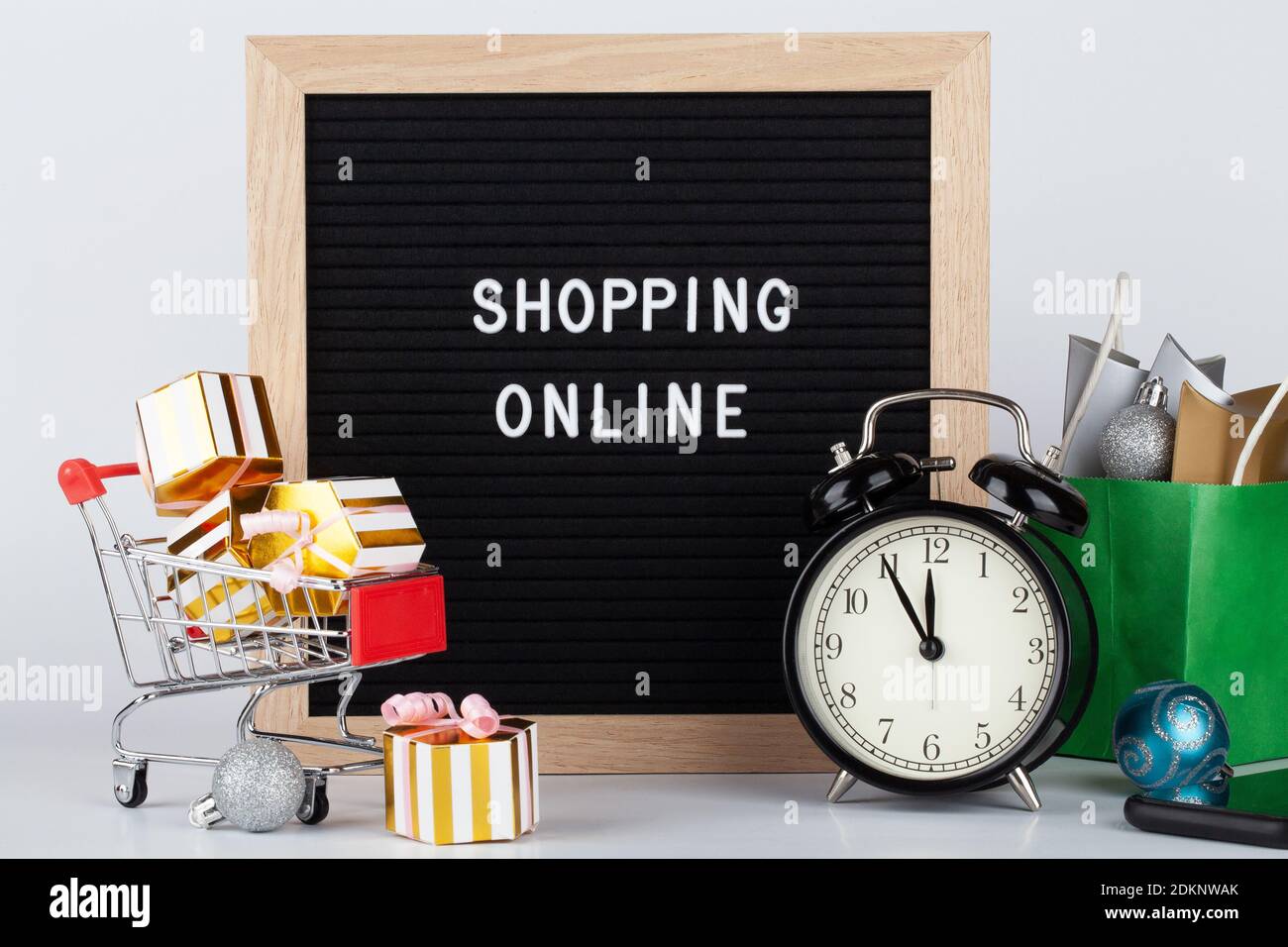 Online, shopping natalizio. Cartellone nero con testo shopping online, carrello con scatole regalo, telefono cellulare e orologio su sfondo bianco. Foto Stock