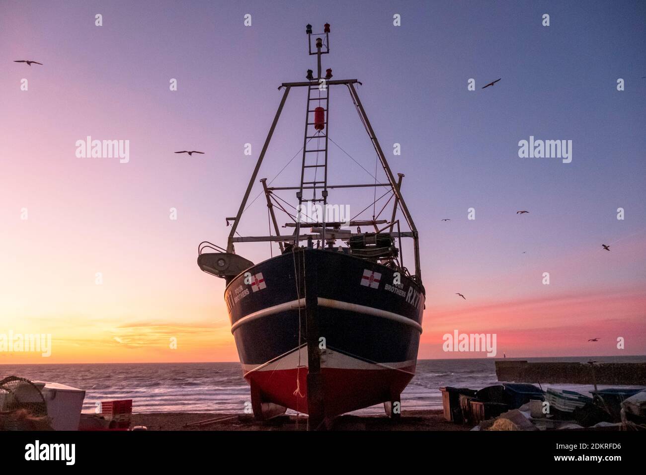 Hastings; East Sussex; UK. 16 dicembre 2020. L'alba è colorata in anticipo mentre i gabbiani si innalzano sopra la barca da pesca in una giornata ventilata ma mite e soleggiata. Carolyn Clarke/Alamy Live News Foto Stock