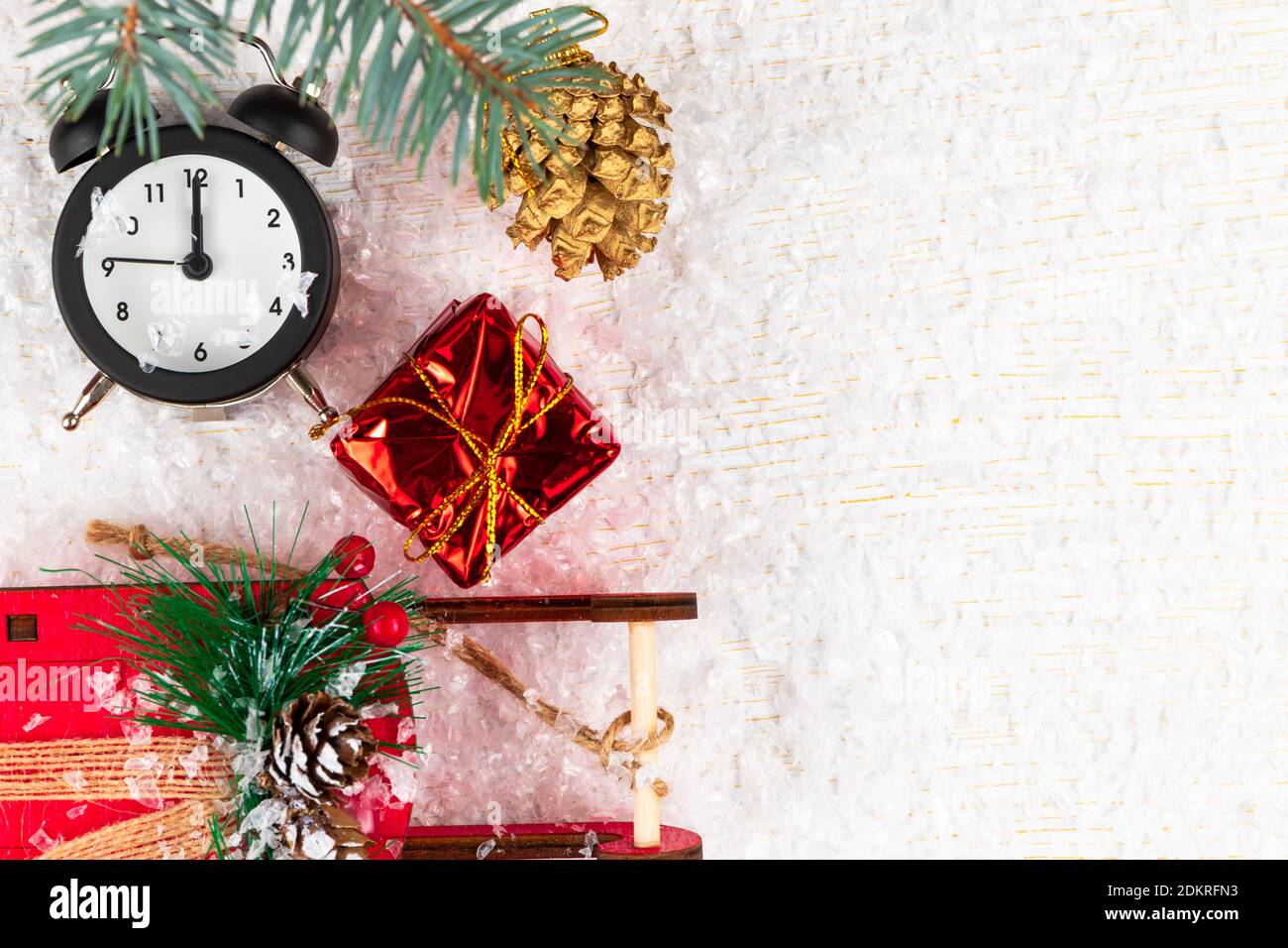 sveglia, slitta babbo natale, una scatola con un regalo, un ramo di albero di Natale e un cono dorato su uno sfondo di legno bianco con venature dorate Foto Stock