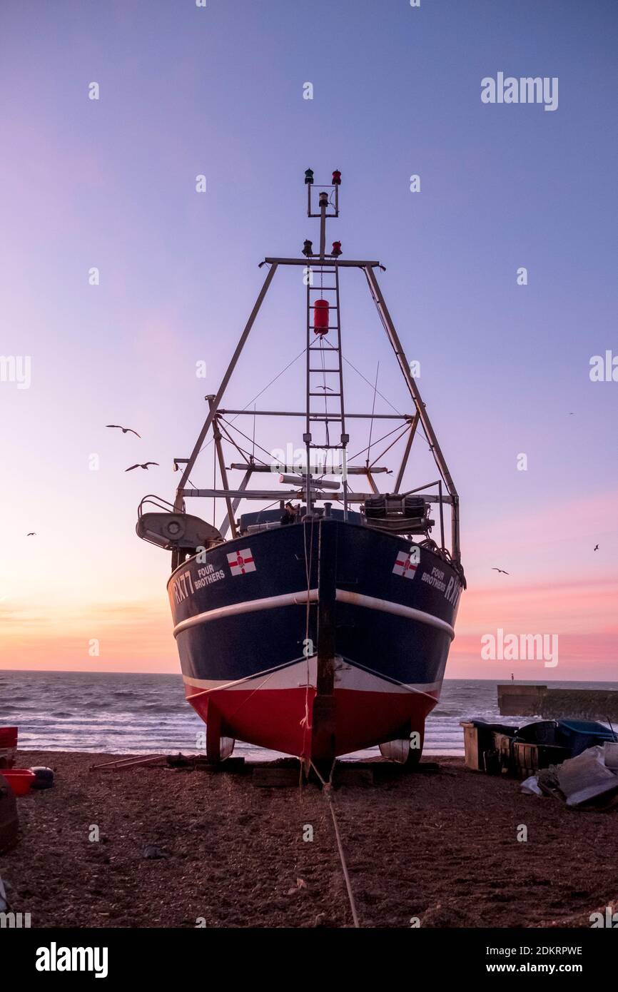 Hastings; East Sussex; UK. 16 dicembre 2020. L'alba è colorata in anticipo mentre i gabbiani si innalzano sopra la barca da pesca, in una giornata ventilata, ma soleggiata e mite. Carolyn Clarke/Alamy Live News Foto Stock