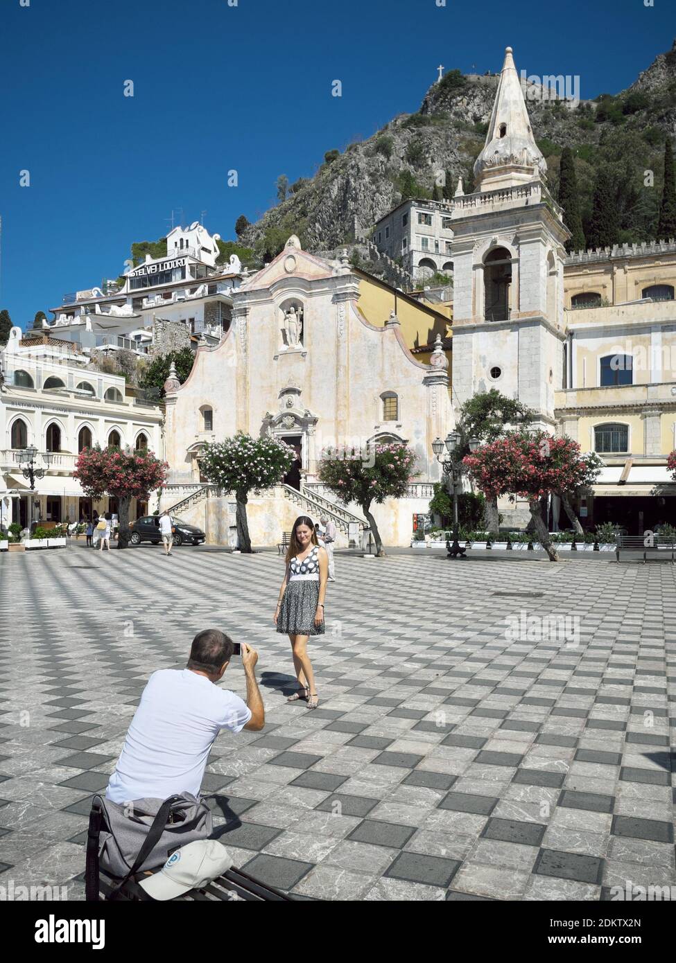 Una coppia scattando foto, la donna che posa per un ricordo fotografico di fronte alla Chiesa di San Giuseppe nel centro storico di Taormina, punto di riferimento turistico della Sicilia Foto Stock