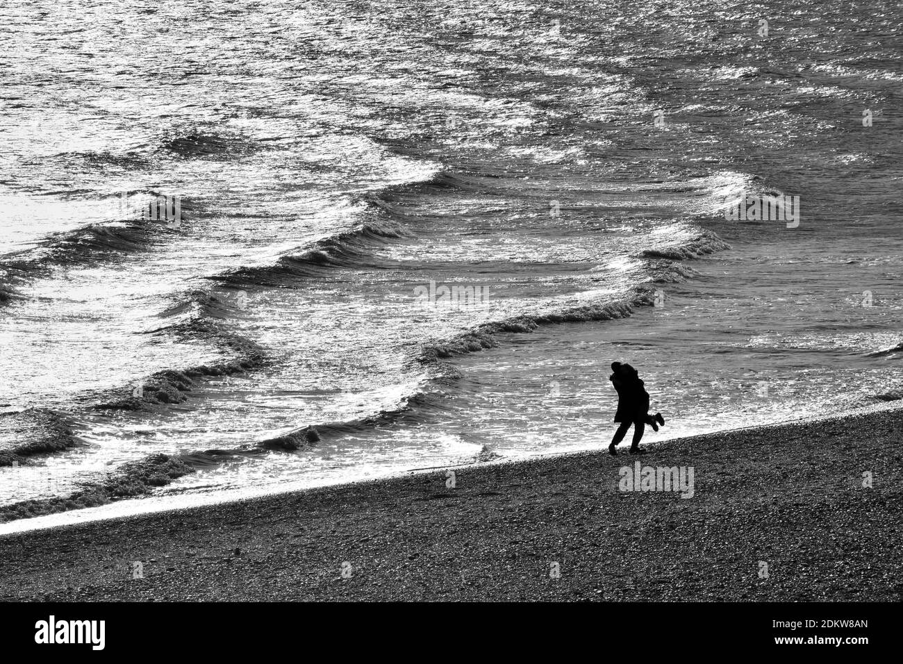 Silhouette di una coppia che si abbraccia su una spiaggia con onde oceaniche durante il lockdown in bianco e nero Foto Stock