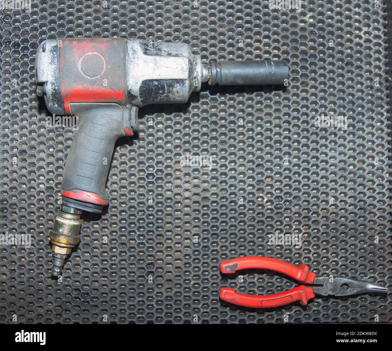 Una vecchia chiave pneumatica sporca e una pinza rossa si trovano sul banco di lavoro di un'officina di riparazione automatica. Primo piano Foto Stock