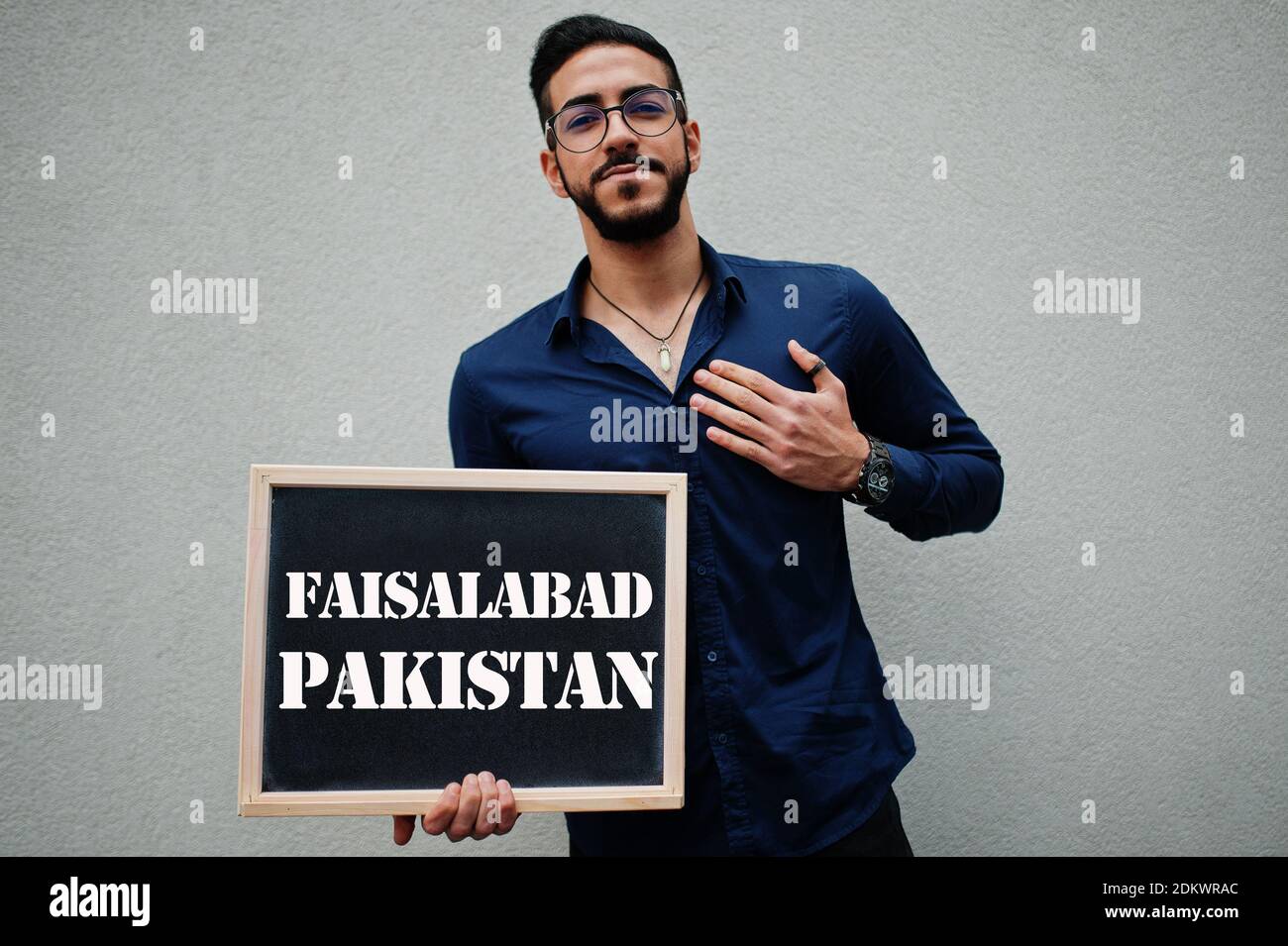 Uomo arabo indossare camicia blu e occhiali tenere tavola con l'iscrizione  Faisalabad Pakistan. Le città più grandi del mondo islamico concetto Foto  stock - Alamy