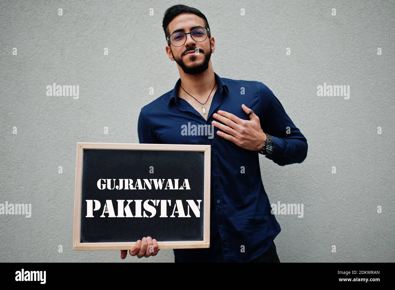Uomo arabo indossare camicia blu e occhiali tenere tavola con iscrizione Gujranwala Pakistan. Le città più grandi del mondo islamico concetto. Foto Stock