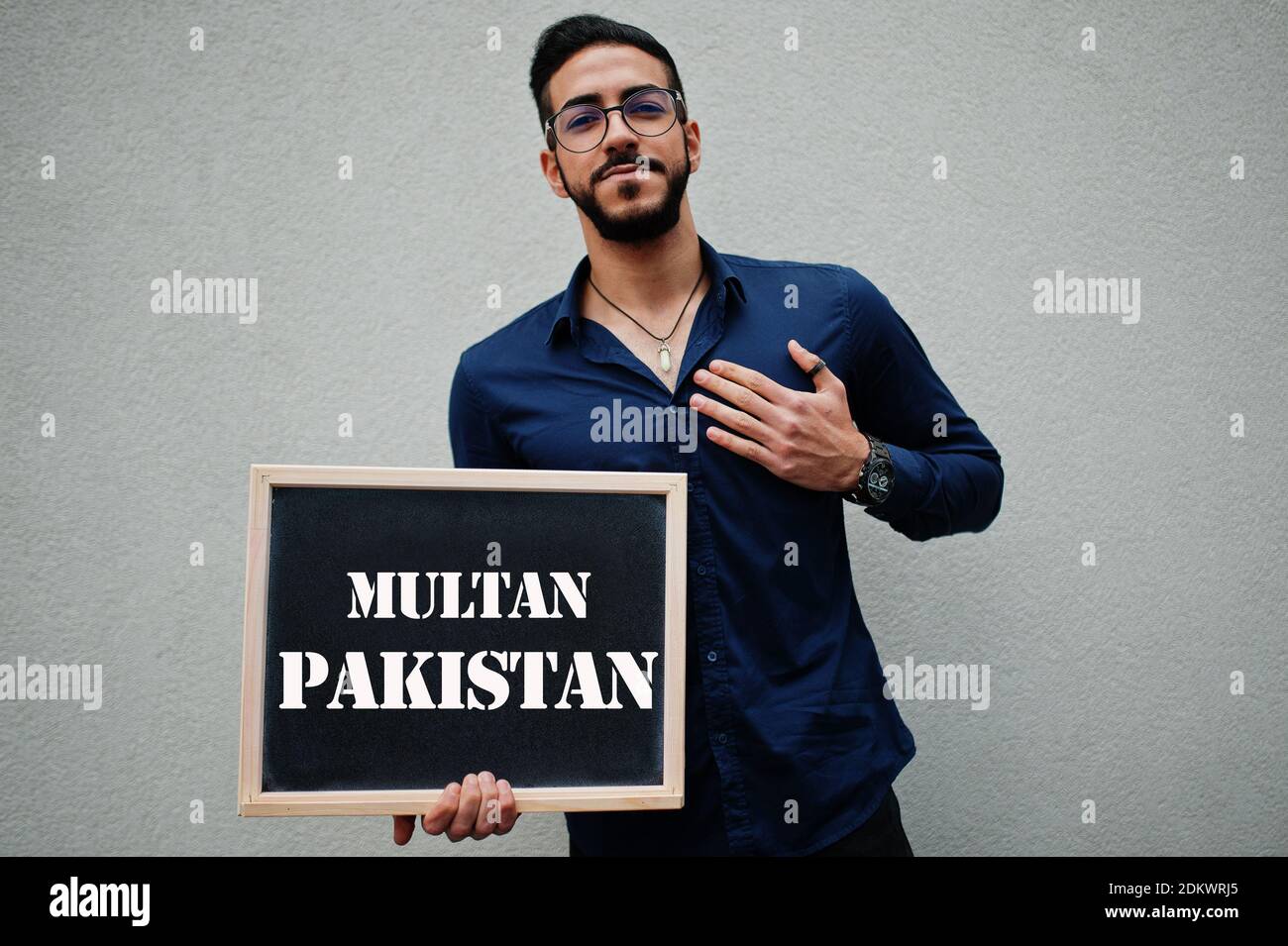 Uomo arabo indossare camicia blu e occhiali tenere tavola con iscrizione Multan Pakistan. Le città più grandi del mondo islamico concetto. Foto Stock